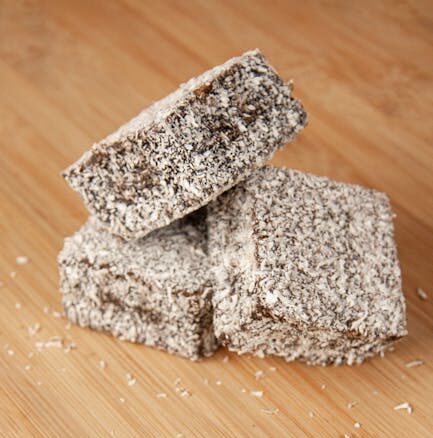 Close-up of three coconut-covered lamingtons on a wooden surface.