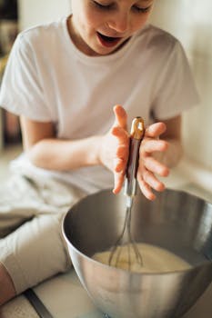 A young boy happily using a whisk in a kitchen, expressing joy and fun while baking.