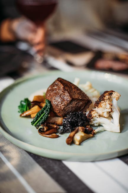 Tasty steak served on plate with white cauliflower and fried mushrooms placed on table in light modern restaurant on blurred background