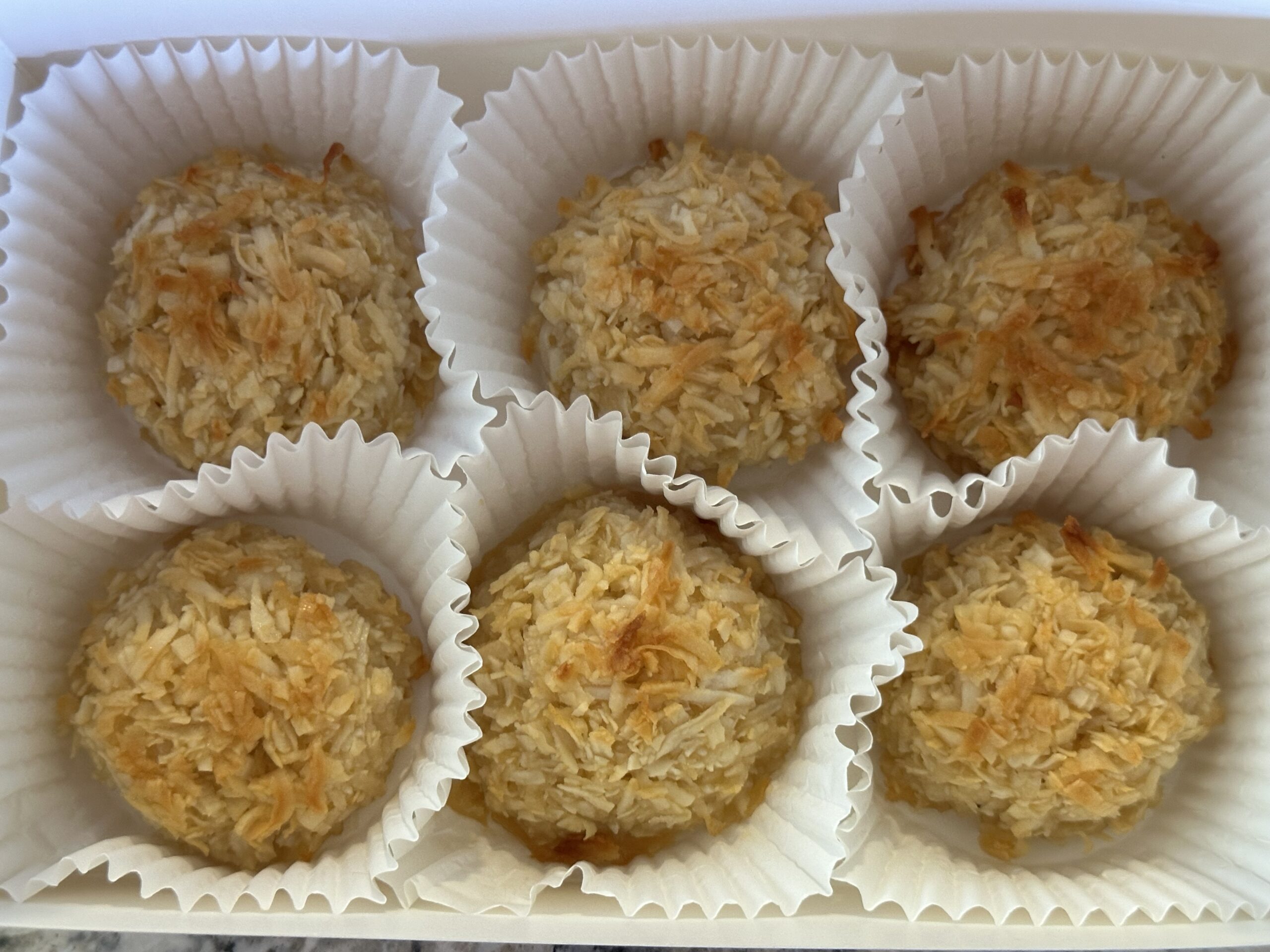 six plain coconut macaroons in individual paper cups in a white bakery box