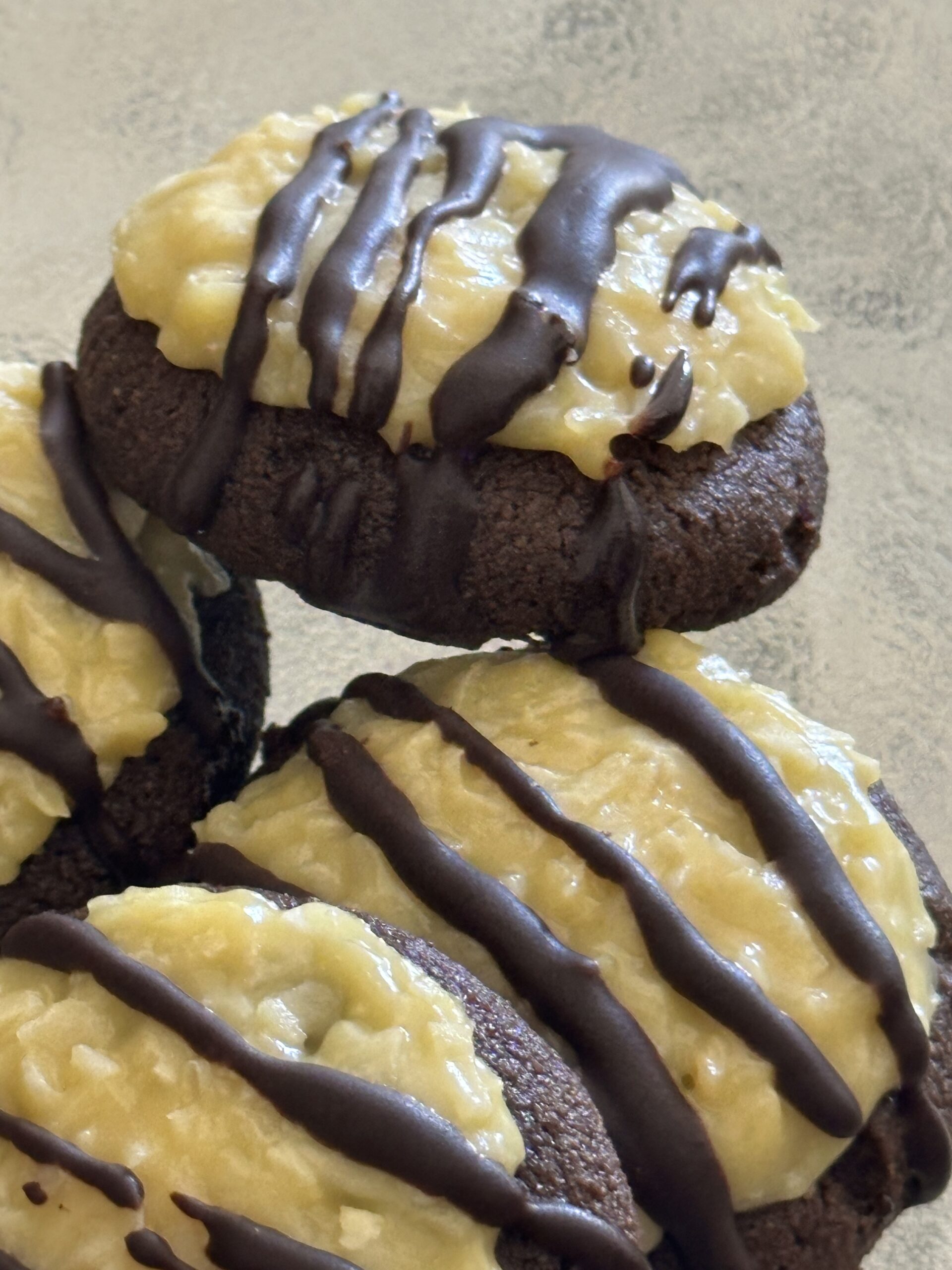 Four German chocolate cookies with coconut topping and chocolate drizzle stacked together